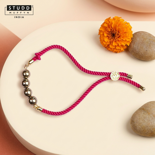 Grounded Grace Rakhi with gold-tone beads on a pink twisted cord, premium festive hero shot
