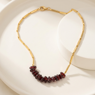 Alchemy Garnet 24K gold-tone rice chain necklace with deep-red crystal chips on a soft white surface
