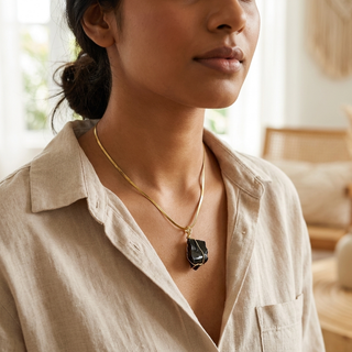 Woman wearing the obsidian pendant on the gold-tone snake chain at her collarbone, no text